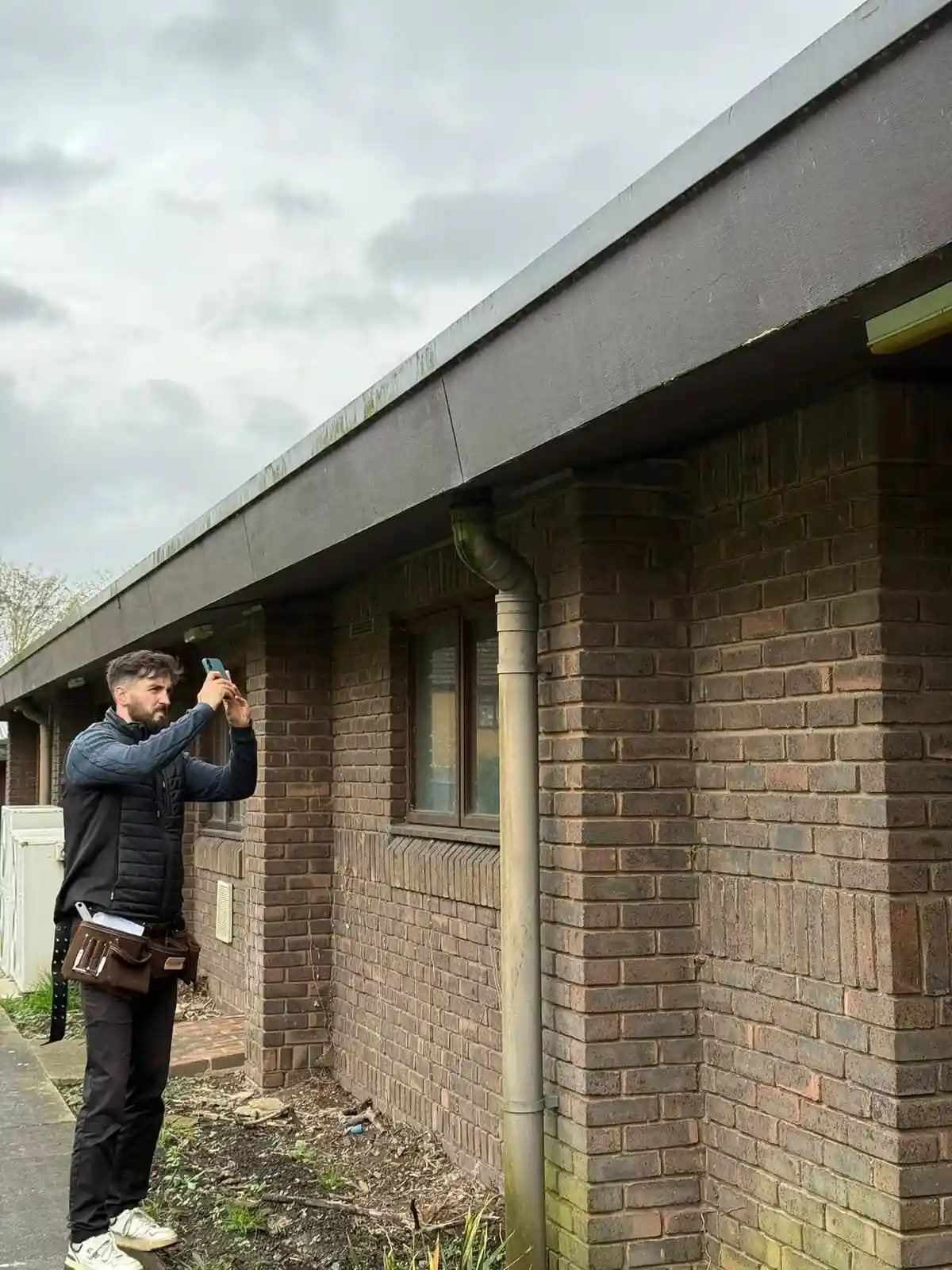 Surveyor taking photos of exterior brickwork and gutters during a condition survey, homebuyer survey, or building survey.