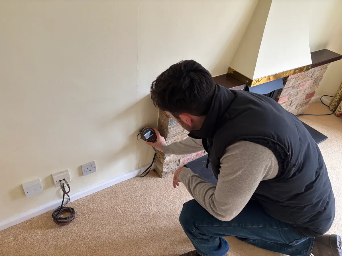 Surveyor using a damp meter near a fireplace during a condition survey, homebuyer survey, or building survey.